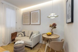 A modern living room with a sofa, a round table with chairs, a hanging light fixture, and two framed artworks on the wall. - Discover this cozy one-bedroom apartment on Calle Blasco de Garay, in the heart of the Chamberí district, one of Madrid's most authentic and traditional neighborhoods. (MADRID)
