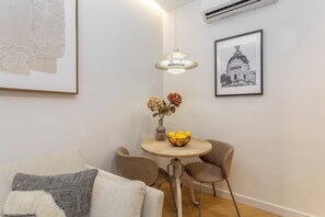 A modern living room with a round wooden table, two chairs, a sofa, a hanging light fixture, and a framed picture on the wall. - Discover this cozy one-bedroom apartment on Calle Blasco de Garay, in the heart of the Chamberí district, one of Madrid's most authentic and traditional neighborhoods. (MADRID)