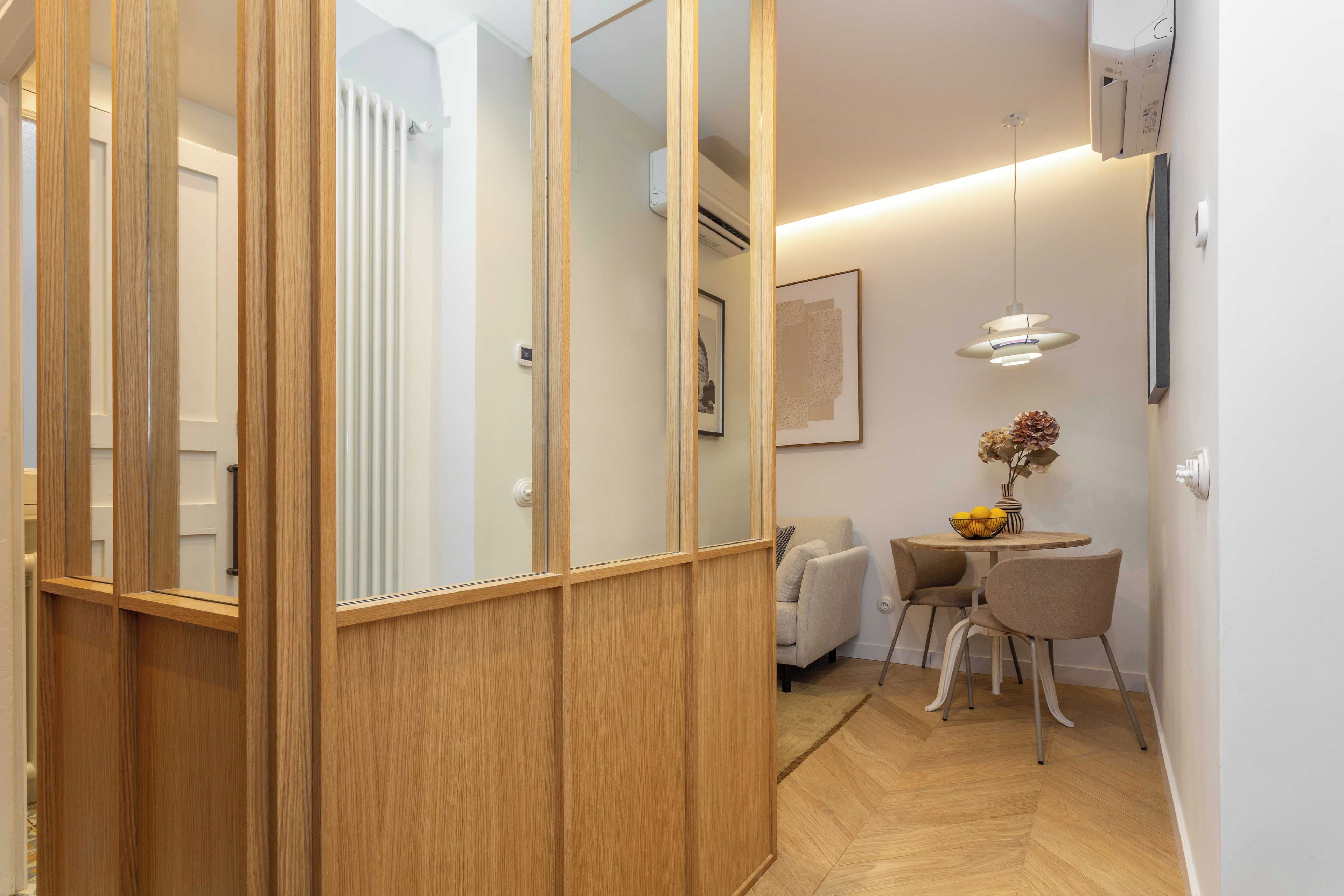 A modern interior with a wooden partition, a dining area with a table and chairs, and a hanging light fixture.