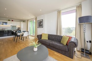 A modern living room with a dark sofa, a round coffee table, and a potted plant. - Comfortable 2BR apartment Deptford Yard, SE8 London - Pass the Keys (London)