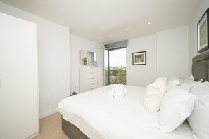 A bedroom with a bed, a dresser, a mirror, a window with a view, and a framed picture on the wall. - Comfortable 2BR apartment Deptford Yard, SE8 London - Pass the Keys (London)