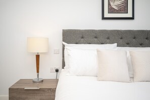 A neatly made bed with white linens and pillows, a bedside lamp, and a framed artwork on the wall. - Comfortable 2BR apartment Deptford Yard, SE8 London - Pass the Keys (London)