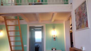 Un interno su più livelli con una scala in legno, un armadietto bianco e una radio a muro.