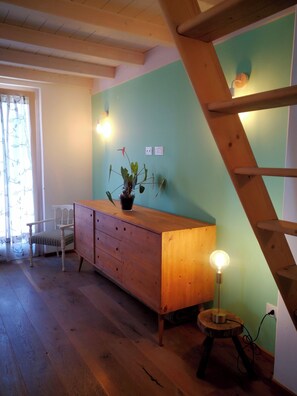 A room with a wooden floor, a wooden bench, a small table with a lamp, and a staircase.