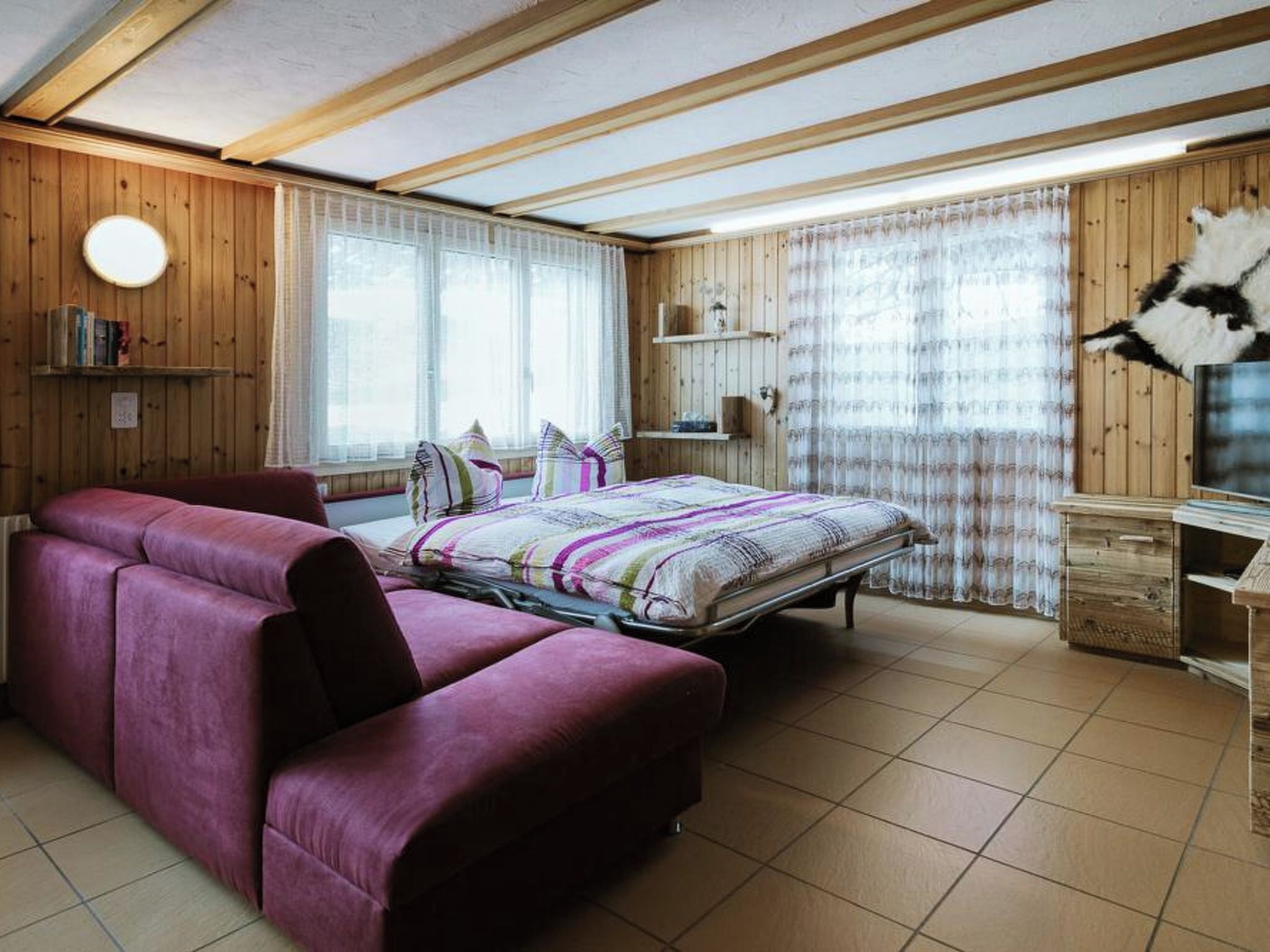 A bedroom with a bed, a sofa, a TV, and wooden walls.