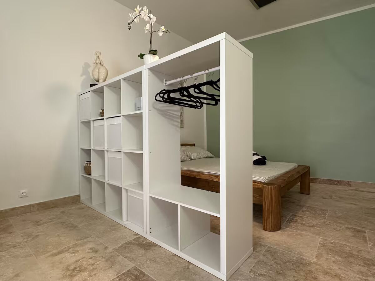Ein Zimmer mit weißem Schrank, einem Bett mit Holzrahmen und einer Kleiderstange.