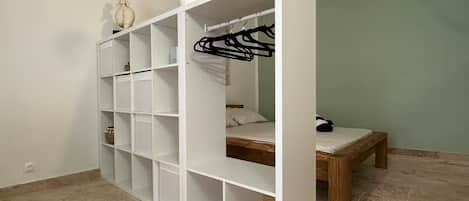 Une pièce avec une armoire blanche, un lit avec un cadre en bois et un portant à vêtements.