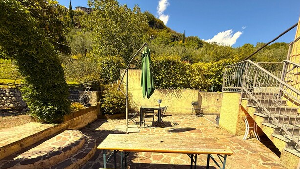 Une terrasse avec une table et des bancs, entourée de murs en pierre et de verdure.