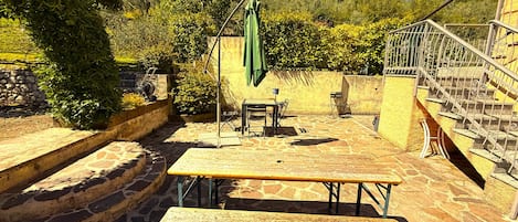 A patio with a table and benches, surrounded by stone walls and greenery.
