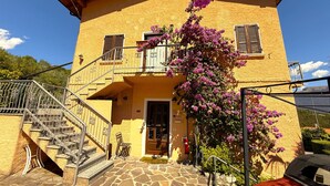 Un bâtiment à deux étages doté d’un escalier en pierre, d’une porte en bois et d’un balcon orné de fleurs violettes.