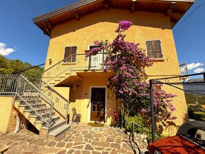 A two-story building with a stone staircase, a wooden door, and a balcony with purple flowers. - Casa Melape Garden & Solarium (Tremosine)