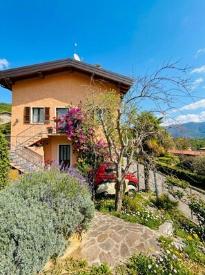 A two-story house with a stone pathway leading to the entrance, surrounded by various plants and flowers. - Casa Melape Garden & Solarium (Tremosine)