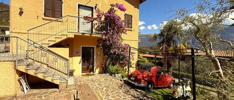 A yellow building with a stone staircase, a wooden bench, and a red car parked outside.