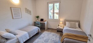 A bedroom with two beds, a desk, a chair, a window, and a bedside table with a lamp. - Casa Melape Garden & Solarium (Tremosine)