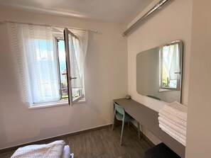 A bedroom with a bed, a desk, a chair, a mirror, and a window with curtains. - Casa Melape Garden & Solarium (Tremosine)