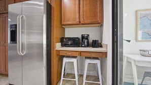Una cuina compacta amb nevera d'acer inoxidable, armaris de fusta, microones i cafetera.