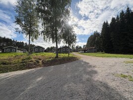 A gravel driveway leading to a row of cabins with a grassy area and trees in the background.