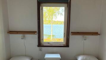 Een kamer met twee eenpersoonsbedden, een klein nachtkastje, een raam met uitzicht op een meer en houten balken aan het plafond.