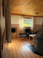 A cozy room with wooden flooring, a television, a leather chair, a small table, and a window with curtains.