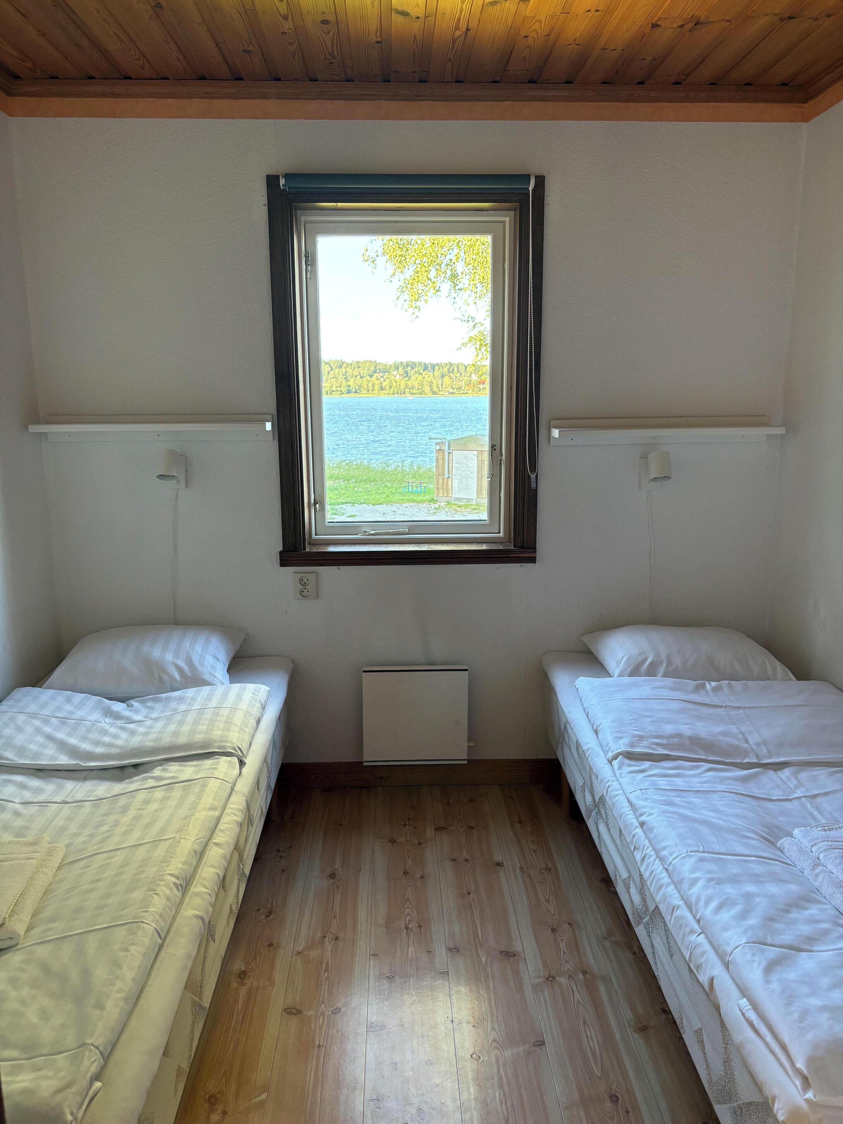 A room with two single beds, a window with a view of a lake, and a white radiator between the beds.