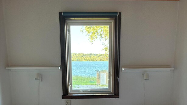 Una habitación con dos camas individuales, una ventana con vistas a un lago y un radiador blanco entre las camas.