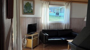 Una habitación con techo de madera, un sofá de cuero negro, un televisor sobre un mueble de madera y una ventana con cortinas.