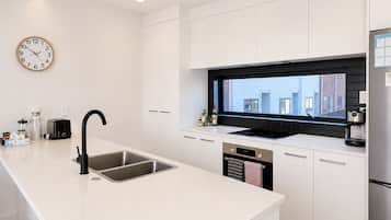 A modern kitchen with white cabinetry, a black backsplash, a stainless steel sink, and a built-in oven.