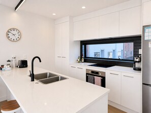 A modern kitchen with white cabinetry, a black backsplash, a stainless steel sink, and a built-in oven.