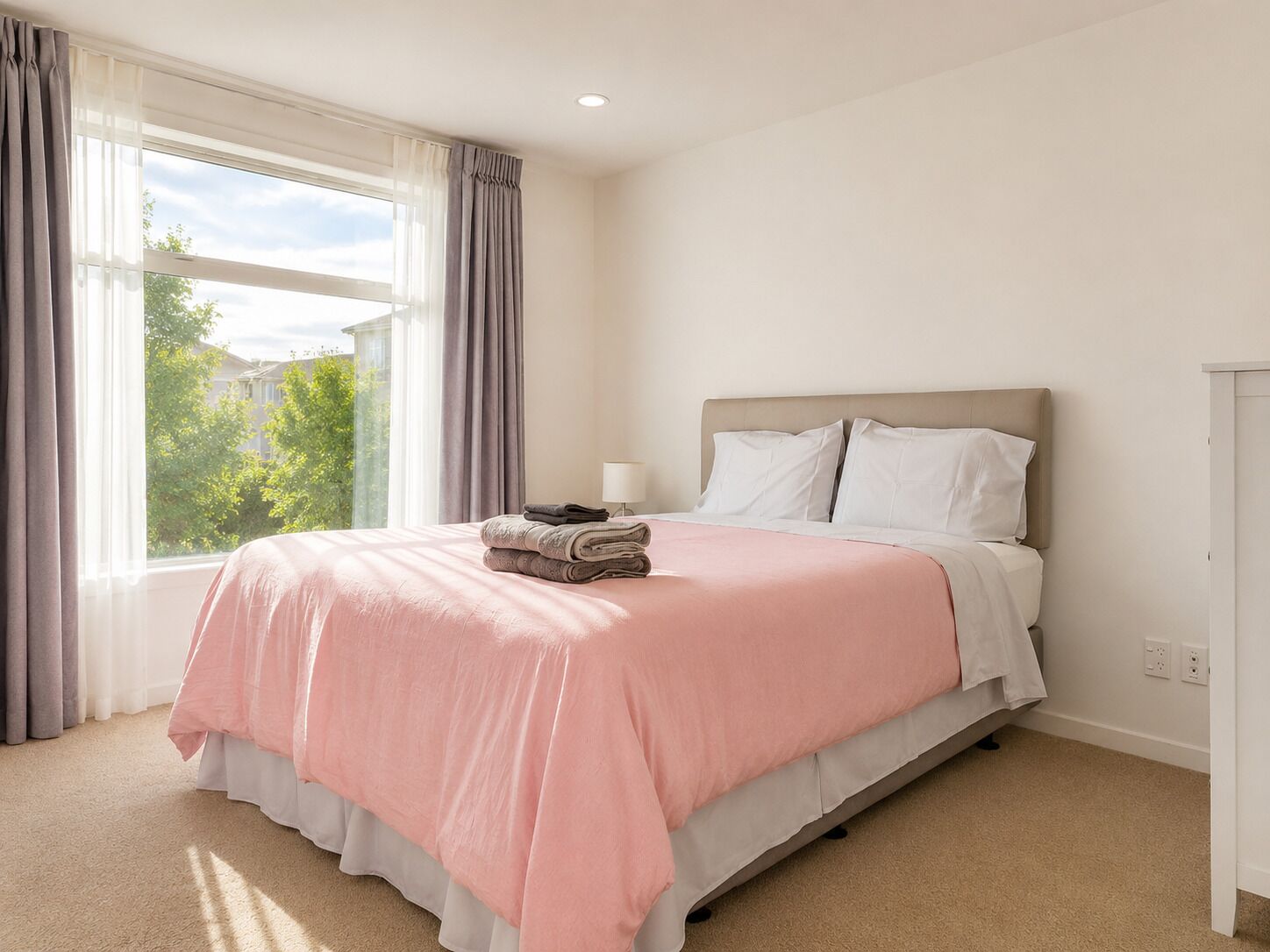 Un dormitorio con cama, ventana con cortinas y vista a zonas verdes.