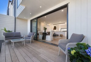 A modern outdoor patio with wicker furniture, a glass table, and a view into the interior.