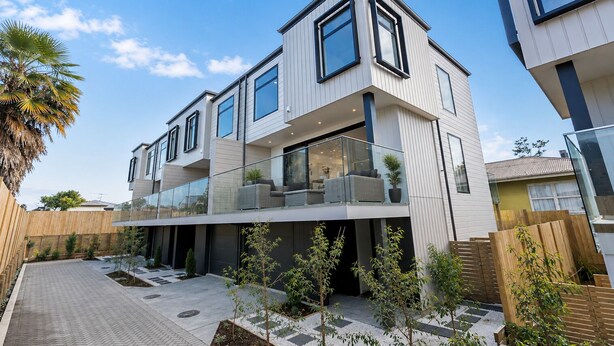 Ein modernes, mehrgeschossiges Wohngebäude mit Balkon, gepflastertem Innenhof und kleinen Bäumen.
