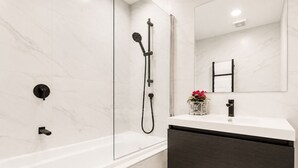 Ein modernes Badezimmer mit einer gläsernen Duschkabine, einem weißen Waschtisch mit dunklem Unterschrank und einem Spiegel über dem Waschbecken.
