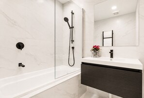 A modern bathroom with a glass-enclosed shower, a white vanity with a dark cabinet, and a mirror above the sink. - Townhouse in Pakuranga (Auckland)