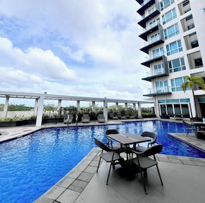 A swimming pool with lounge chairs and tables, a white bridge, and a modern building with balconies. - Room-your Next Iloilo Escape Starts AT O (Iloilo)