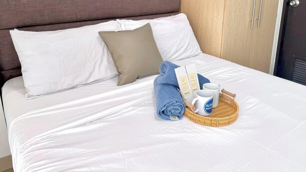 A neatly made bed with white linens, a beige pillow, a blue towel, and a tray with a mug and a bottle.