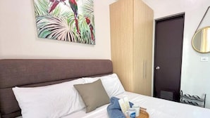A neatly made bed with white linens, a brown headboard, and a tropical bird painting above it.