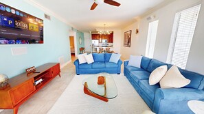 A living room with a blue sofa, a glass coffee table, and a wooden side table. - The "Look Out" @Dolphin Point. Renovated Penthouse (Destin)