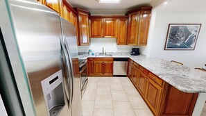 A kitchen with wooden cabinets, a stainless steel refrigerator, a dishwasher, and a granite countertop. - The "Look Out" @Dolphin Point. Renovated Penthouse (Destin)