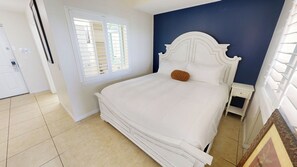 Um quarto com uma cama, janela, porta e mesa de cabeceira.