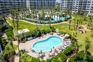 A large swimming pool surrounded by palm trees and lounge chairs, with a view of high-rise buildings in the background. - Beautiful Beachside Studio DW V504 (Fort Walton Beach)