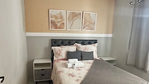 Ein aufgeräumtes Schlafzimmer mit einem Bett, Nachttischen, einer Nachttischlampe und einem Wandbild.