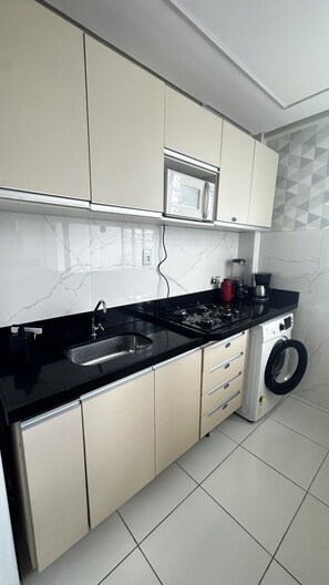 A modern kitchen with a black countertop, a built-in microwave, a gas stove, a sink, and a washing machine. - 305 2 Qtos - 15 min Centro (Belém)