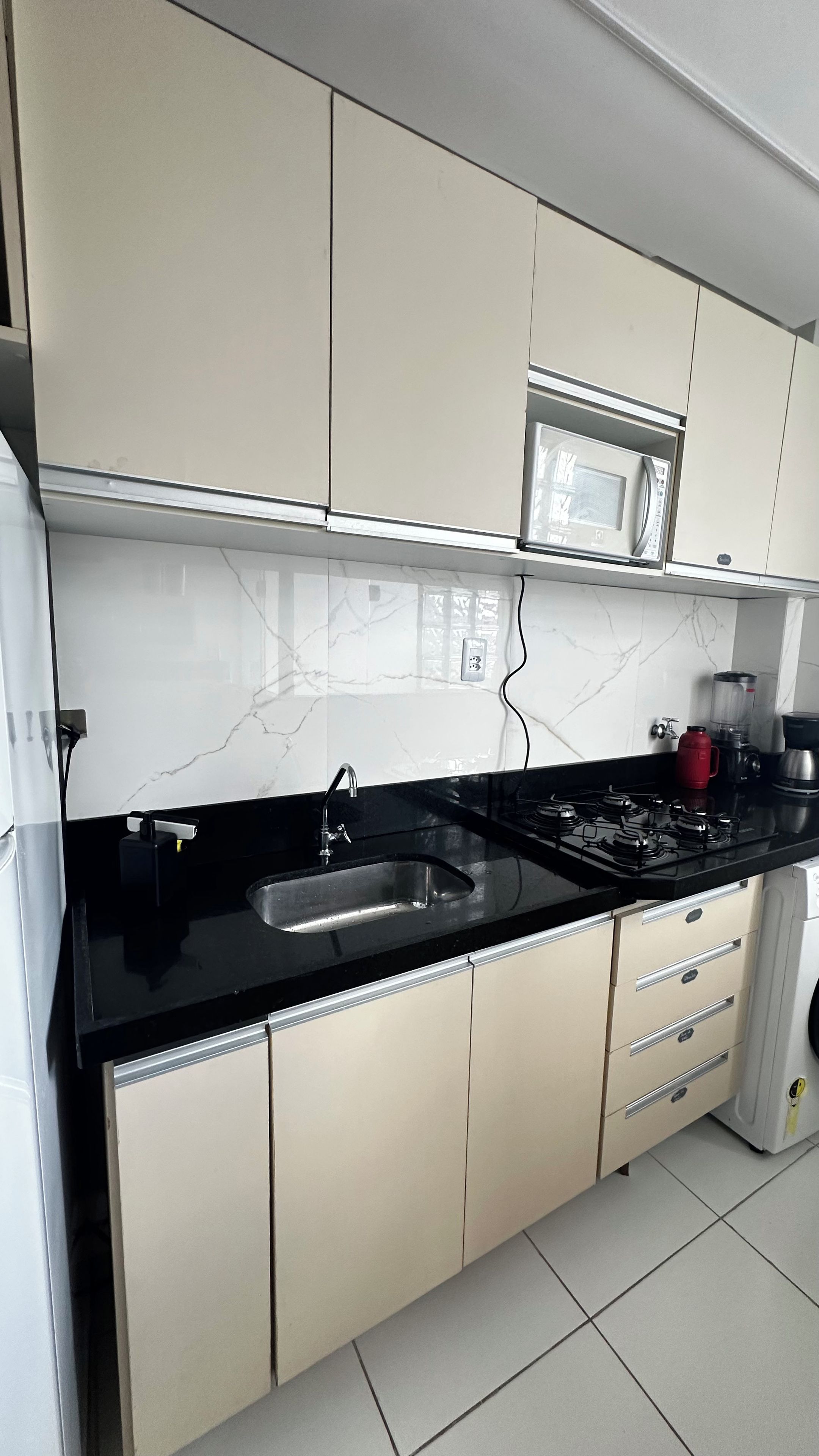 Una cocina moderna con encimera negra, armarios blancos, microondas integrado y cocina a gas.