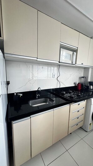 A modern kitchen with a black countertop, white cabinets, a built-in microwave, and a gas stove. - 305 2 Qtos - 15 min Centro (Belém)