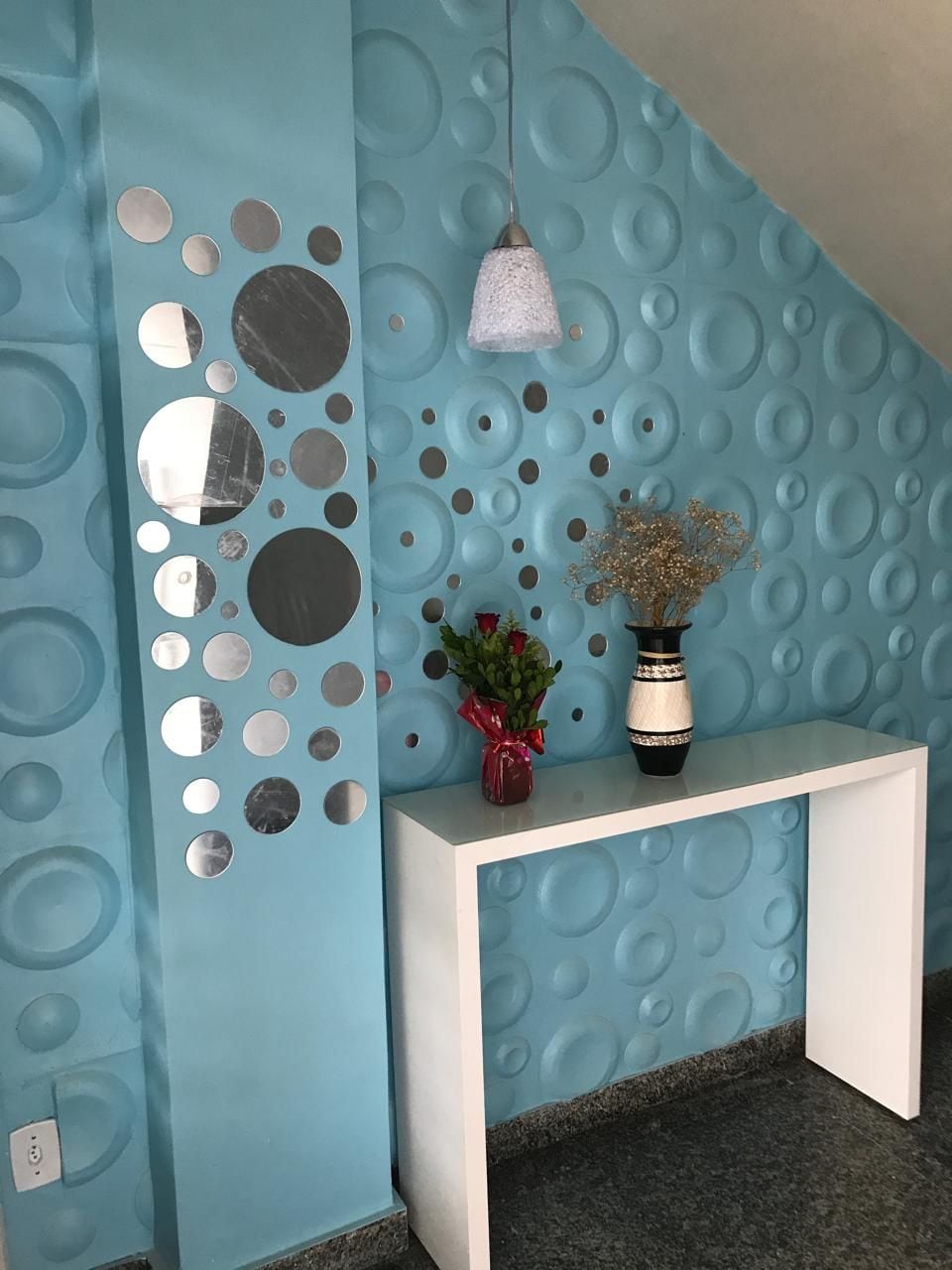 Zona de recepción con pared azul con textura, una mesa consola blanca y una lámpara colgante.