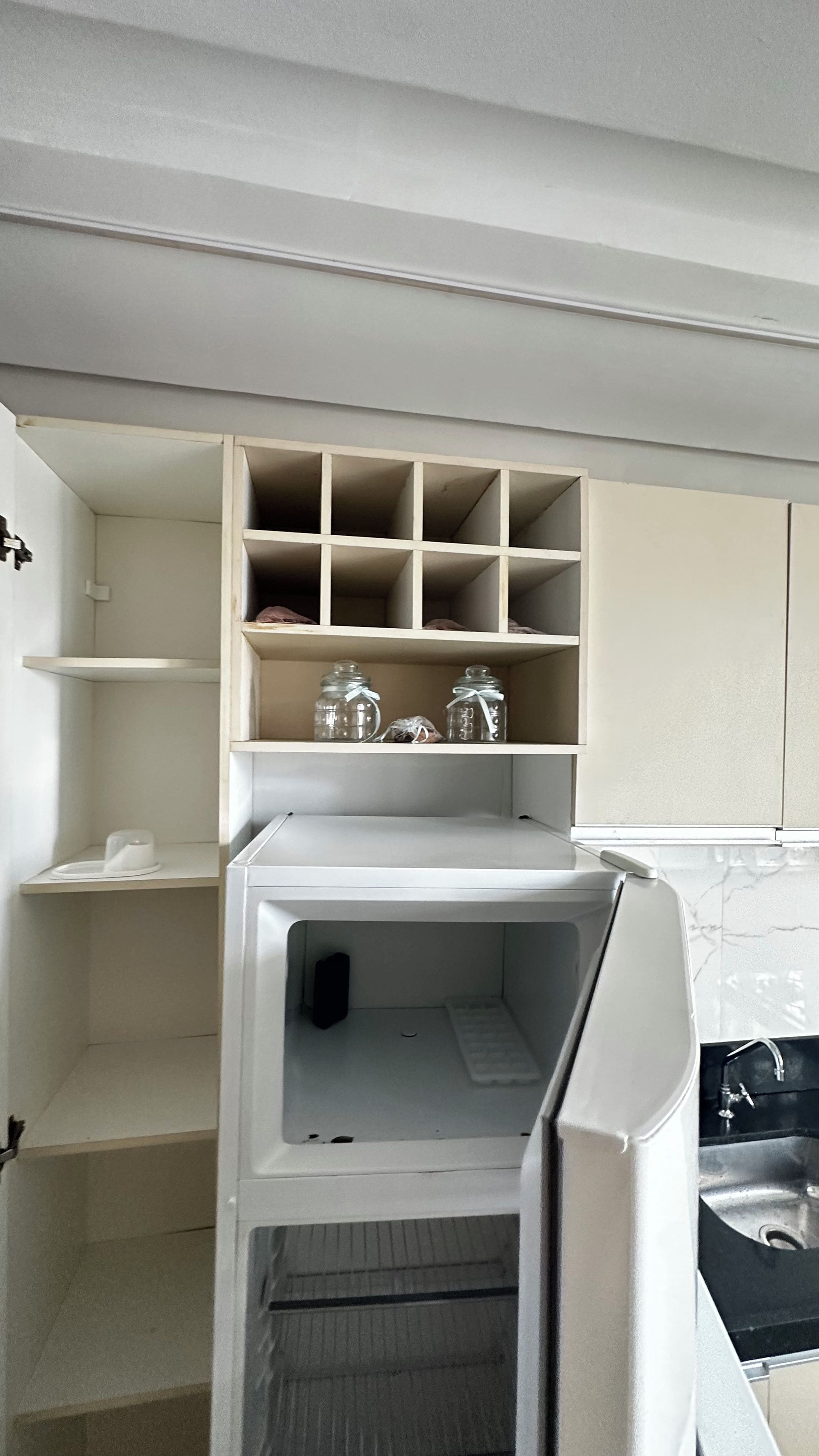Una cocina con un refrigerador blanco, una estantería empotrada arriba y una encimera negra con un lavamanos.