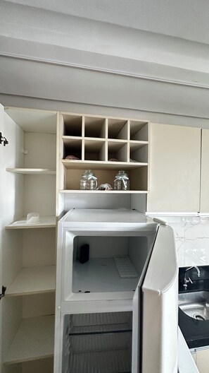 A kitchen with a white refrigerator, a built-in shelf unit above it, and a black countertop with a sink. - 305 2 Qtos - 15 min Centro (Belém)