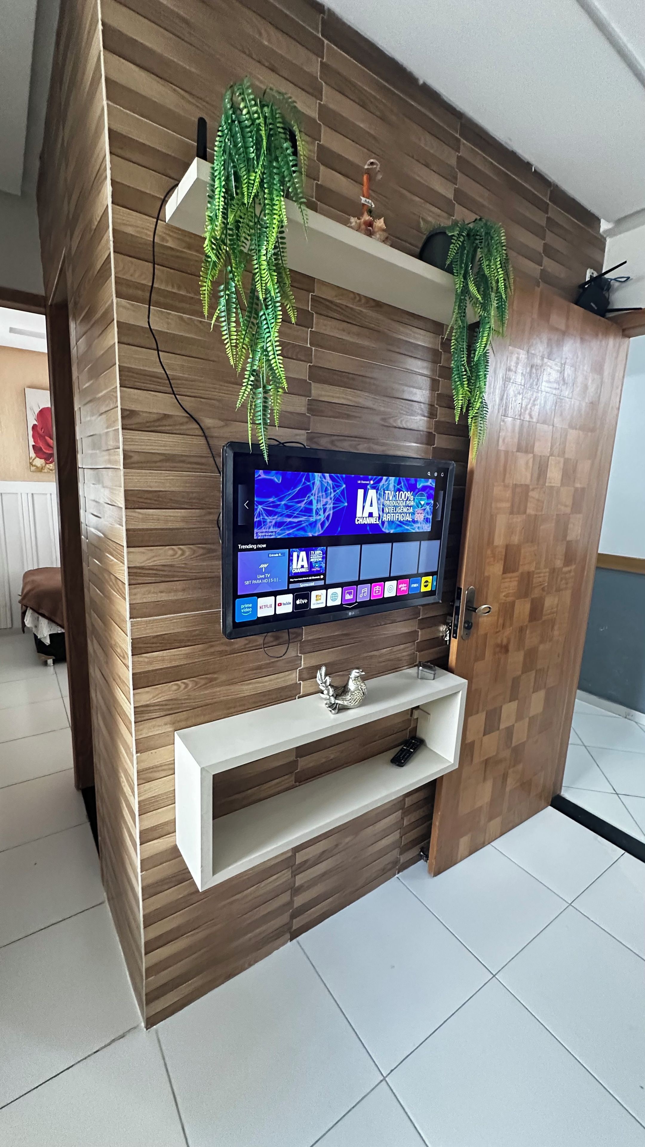 Una sala moderna con un televisor de pantalla plana montado en una pared de madera, una consola blanca debajo y plantas decorativas colgantes.
