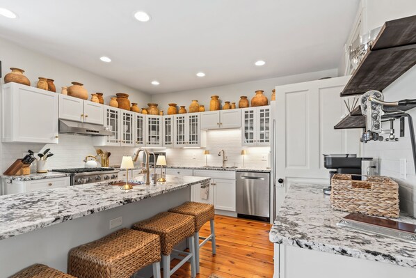 A modern kitchen with white cabinetry, a marble countertop, and a central island with bar stools.