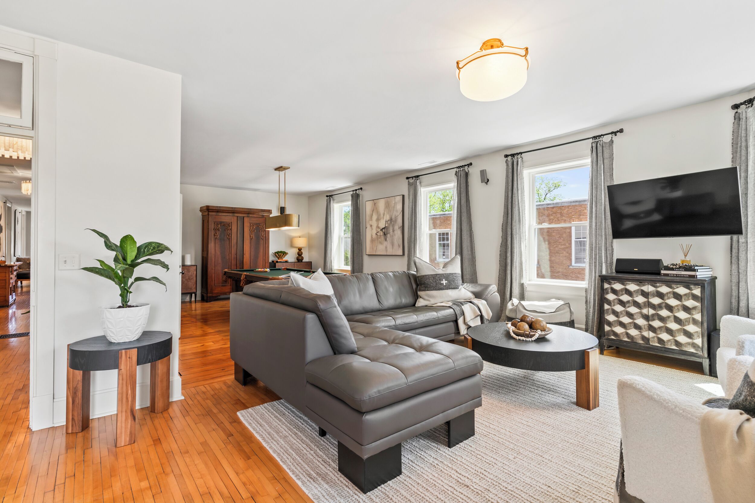 A modern living room with a sectional sofa, a dining area with a pool table, and a kitchen in the background.